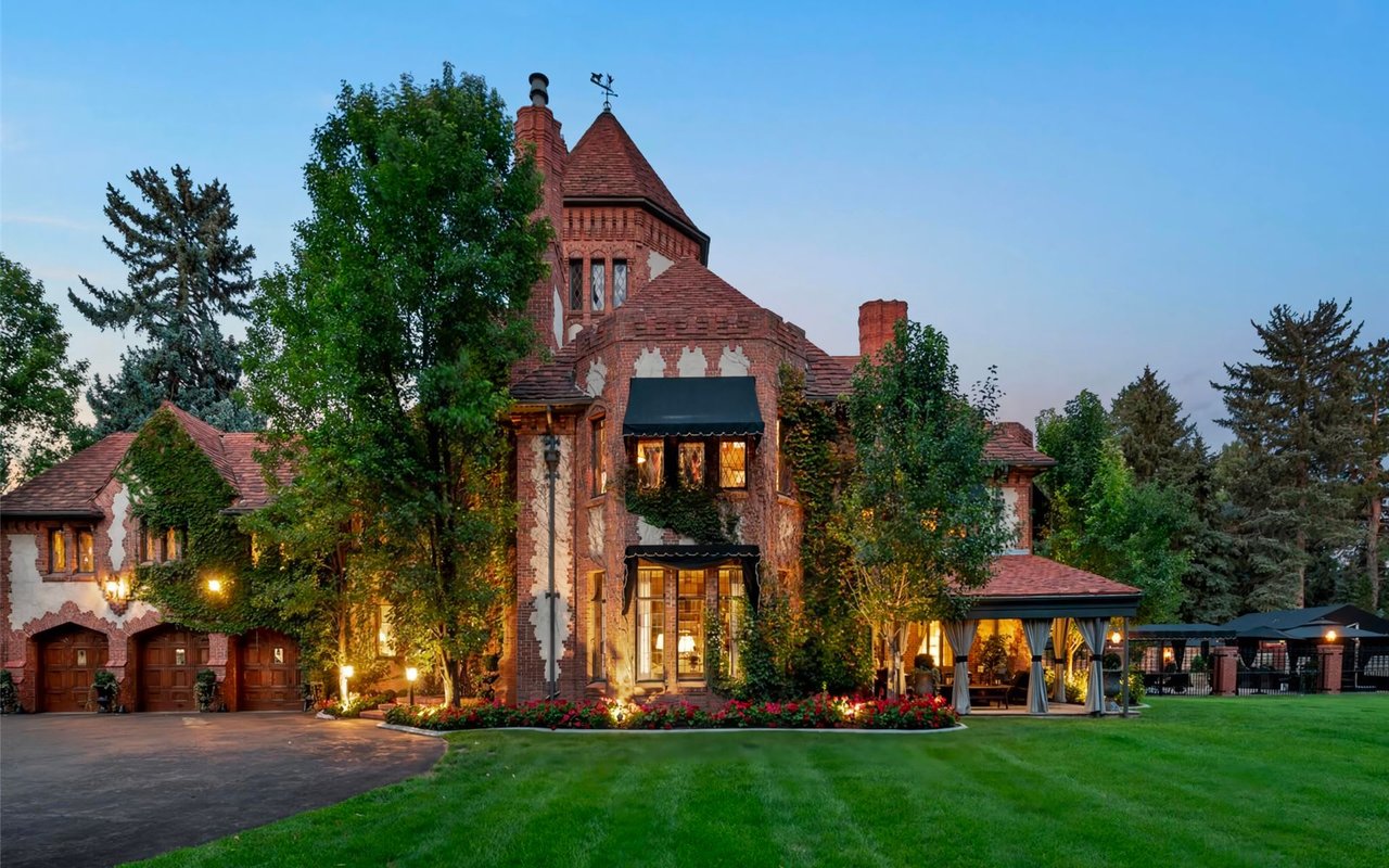 A large brick house with a symmetrical design. It has a big lawn in front of it and is surrounded by mature trees.