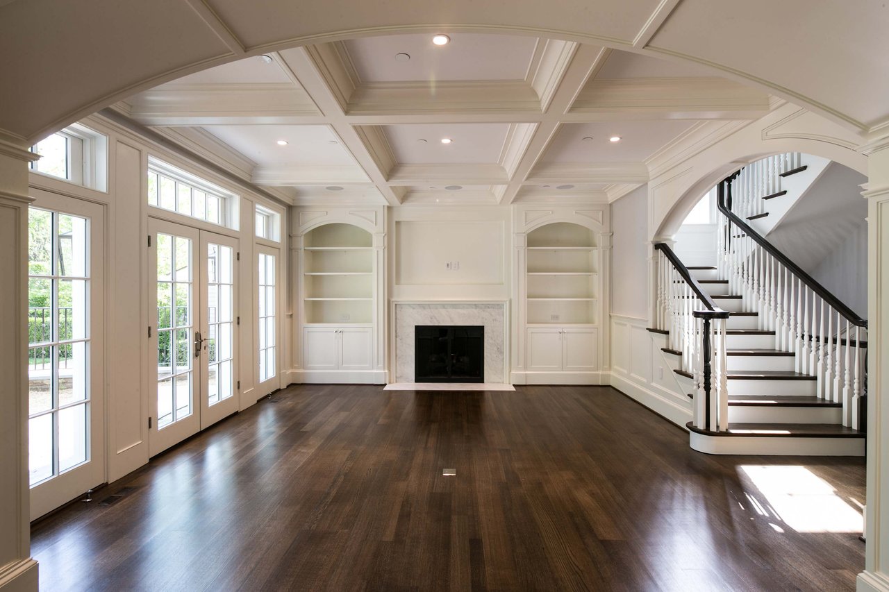 Luxury custom home living room in Maryland with coffered ceiling, fireplace, and curved staircase