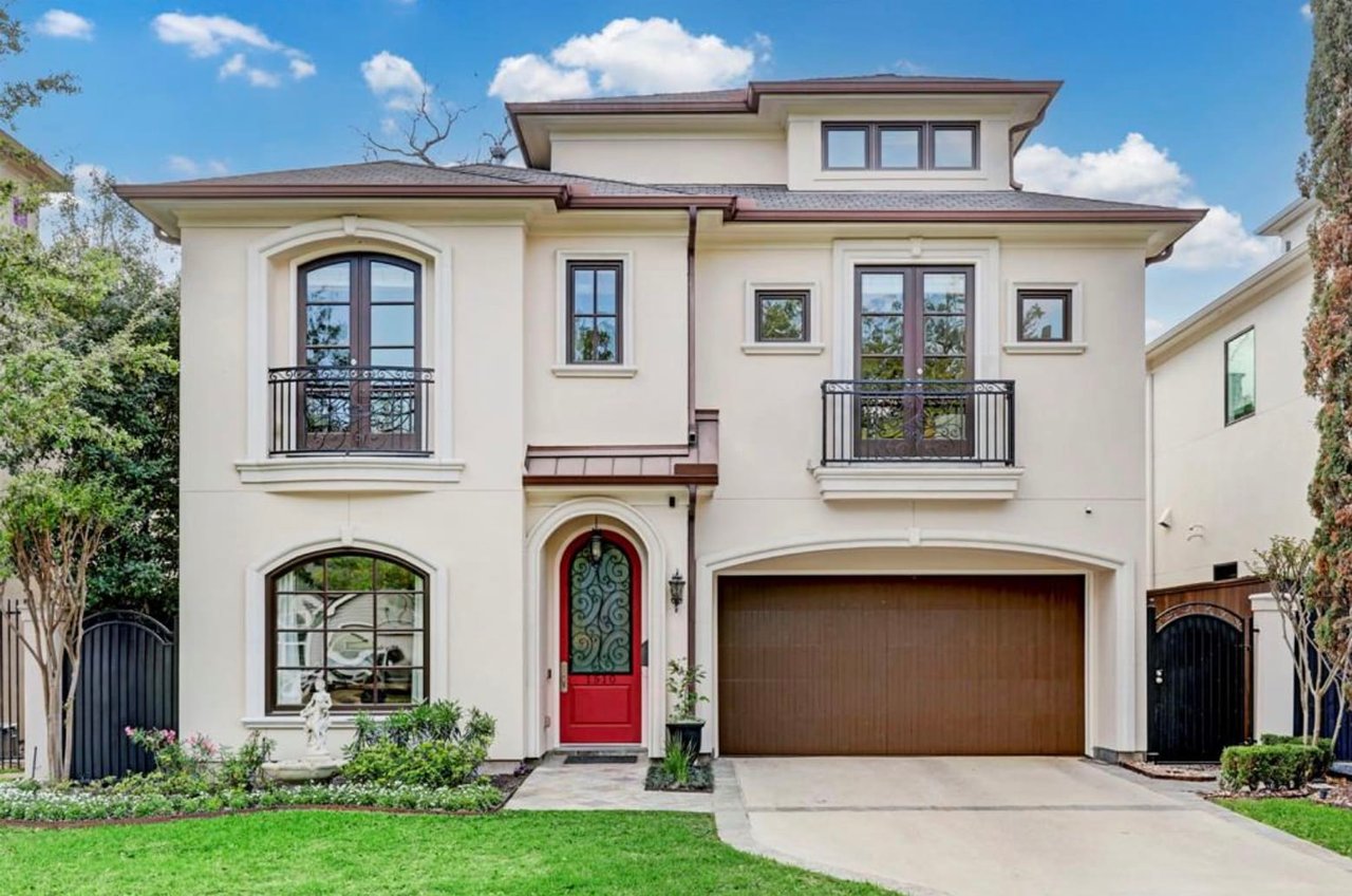 A single-story suburban house with a white exterior, red door, covered porch, two-car garage, and manicured front lawn.