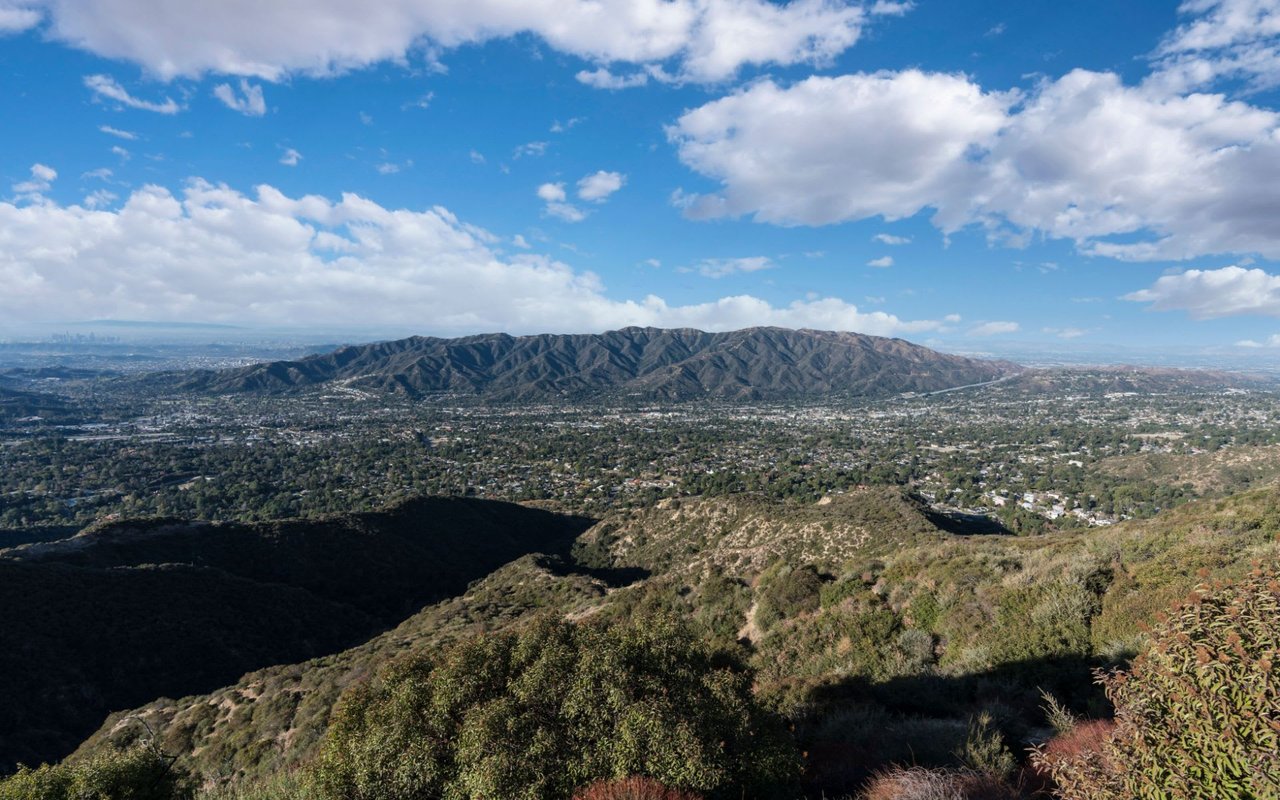 City nestled in lush mountains under a blue sky with white clouds and densely packed houses in the foreground.