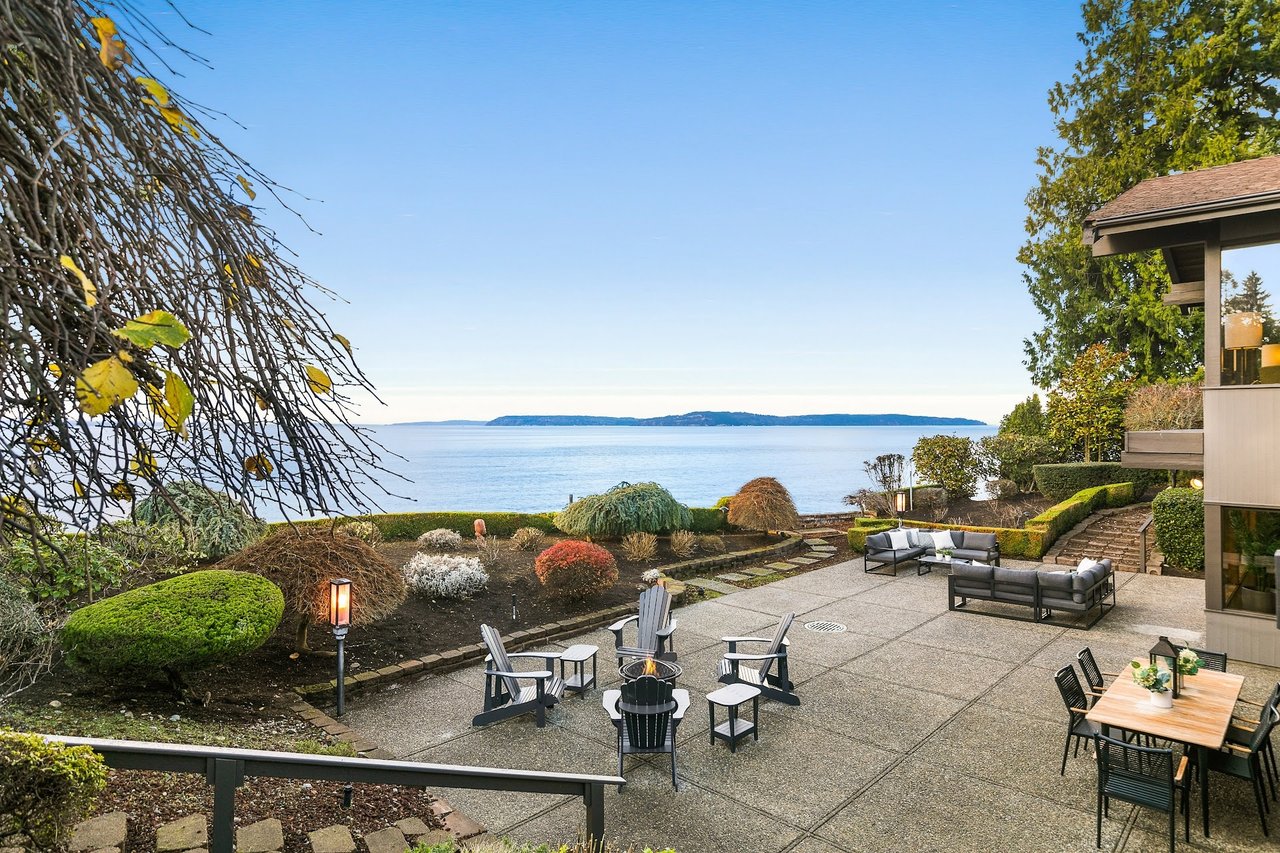 A large patio with a fire pit, table, and chairs overlooking the ocean.