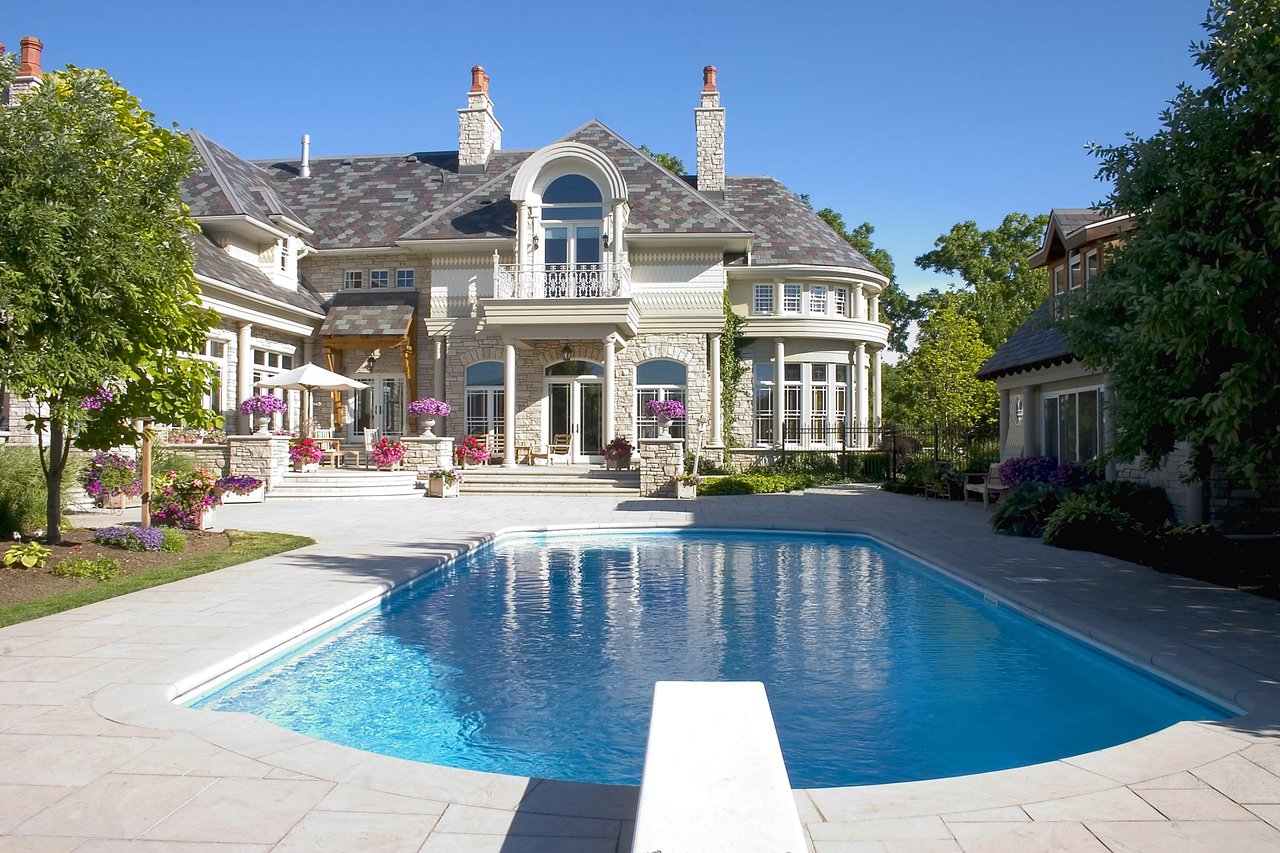 Backyard of a luxury home with pool and diving board in the foreground