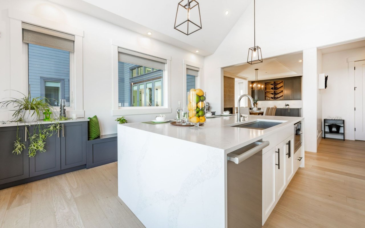 A large, modern kitchen with a central island, a dining area to the left, and windows with views of a patio or deck.