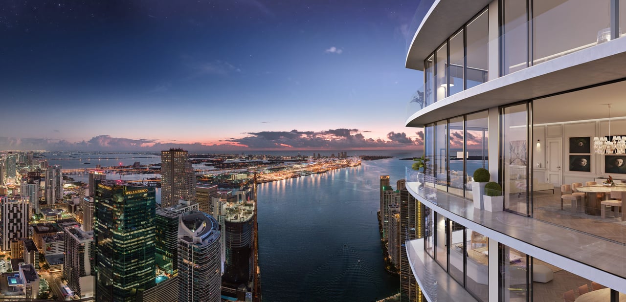 Baccarat’s curved glass high-rise overlooks a bay and illuminated city skyline at dusk.