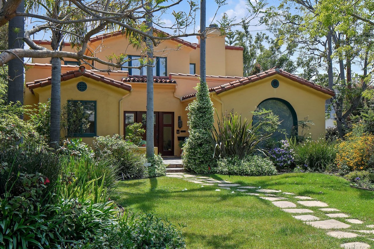  A warm, inviting Spanish-style house with yellow stucco walls and a red tile roof is nestled amongst lush green landscaping 
