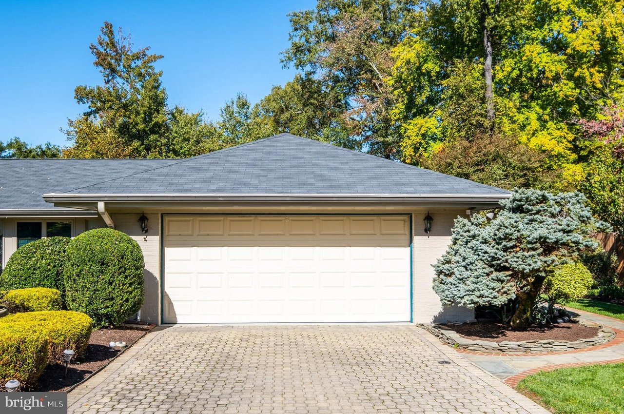Home exterior with a white double garage, wide paved driveway, and neatly trimmed shrubs.