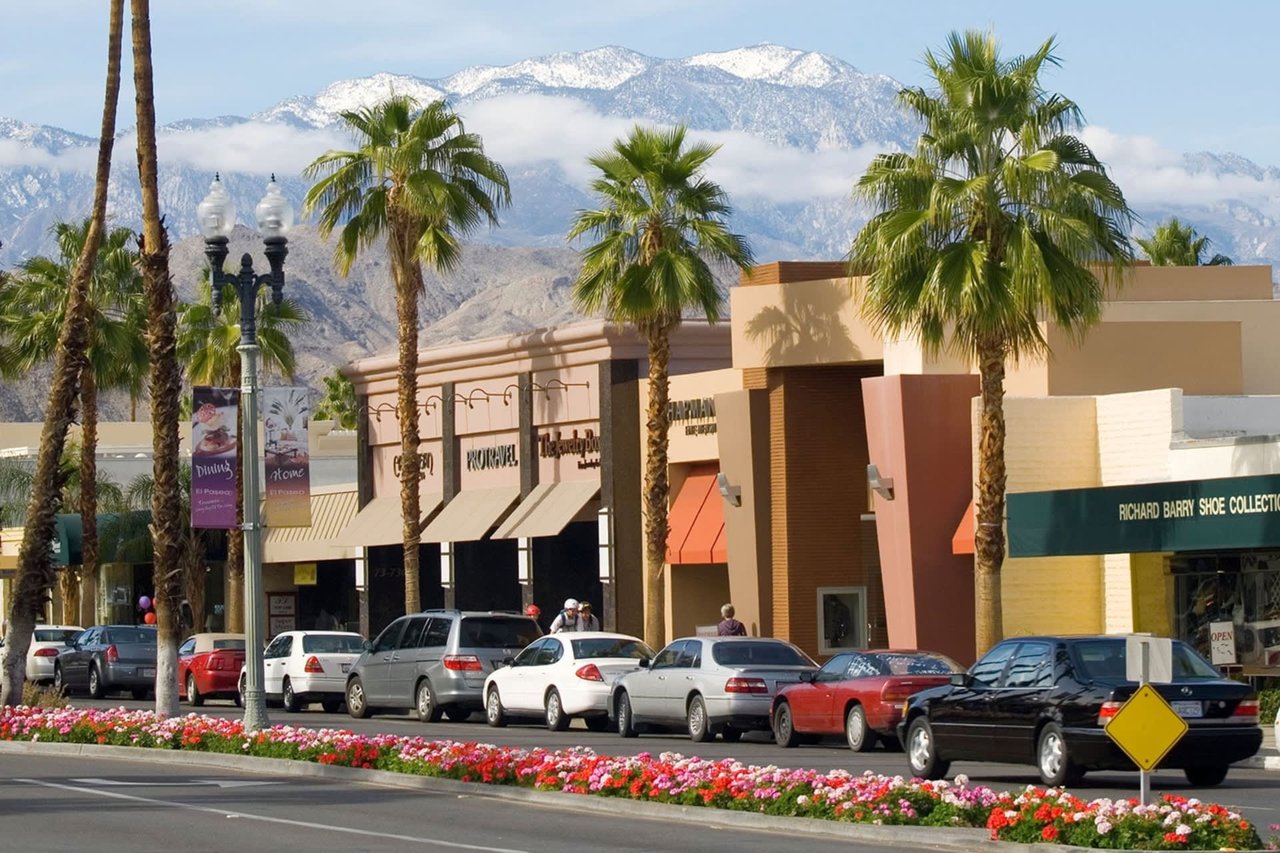 A row of cars parked along a street with a mountain range in the background.