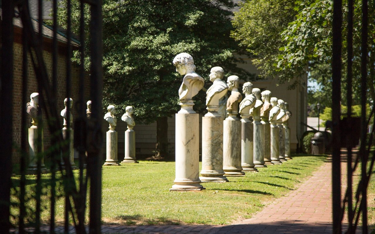 A row of marble busts sitting on top of pillars in a park