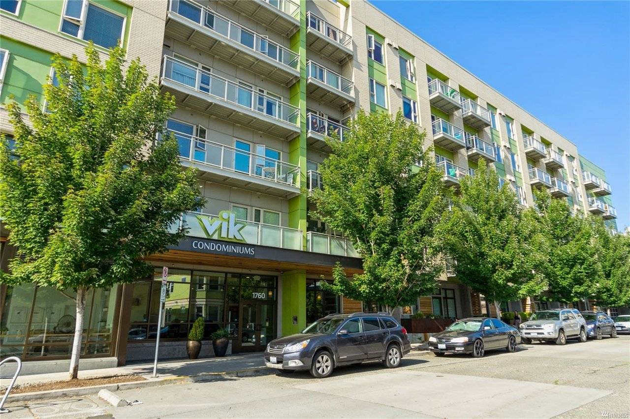  Street-level view of a vibrant and modern condominium complex with lush greenery on a sunny day.