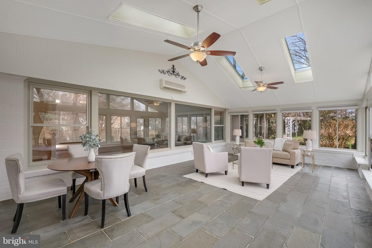 Furnished sunroom with skylights, ceiling fans, large windows, and a gray tile floor.