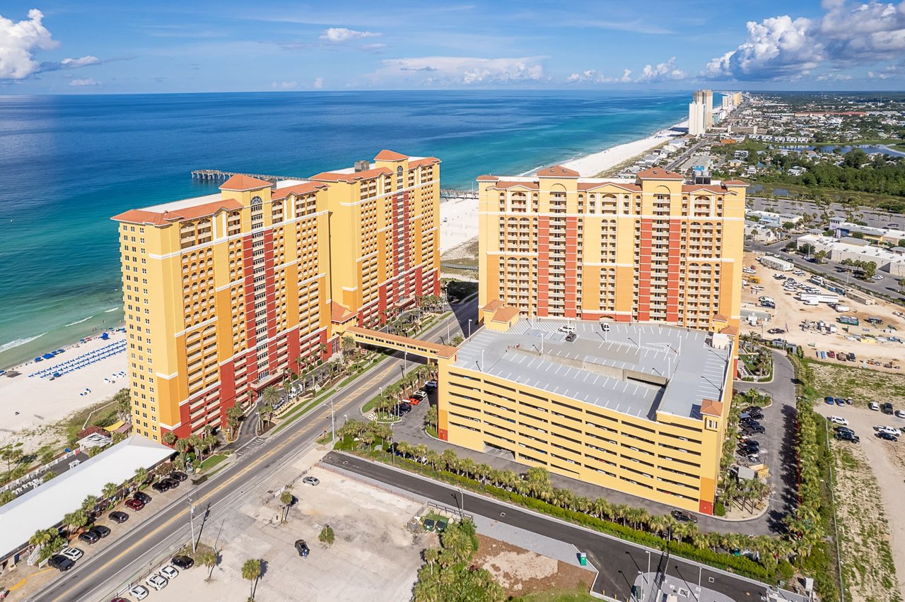 An aerial view of the Panama City Beach high-rise Calypso Towers, parking structure and turquoise waters of the beach.