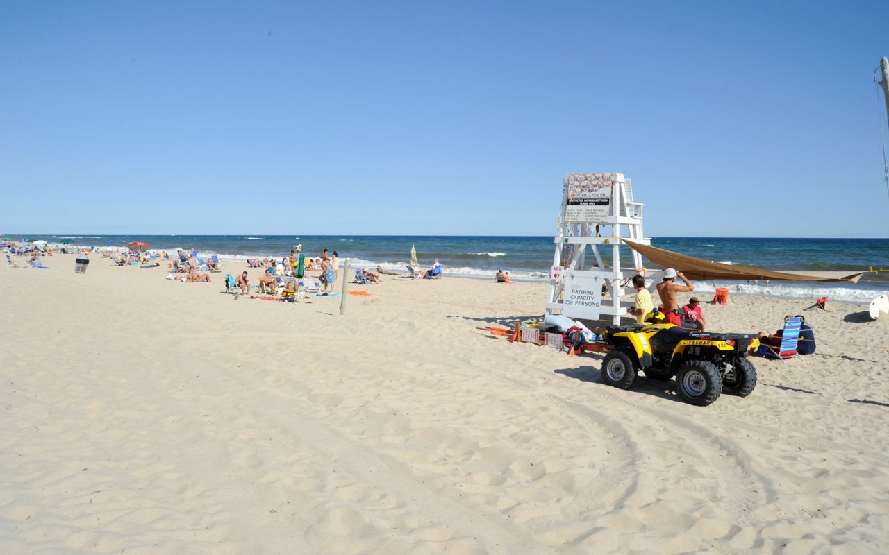 A sunny beach scene with people enjoying the sand and water, accompanied by a lifeguard tower.