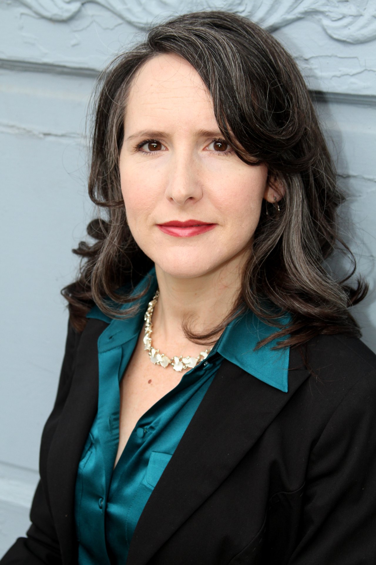 Wendy Longerbeam in a teal blouse and black blazer against a pale blue wall.