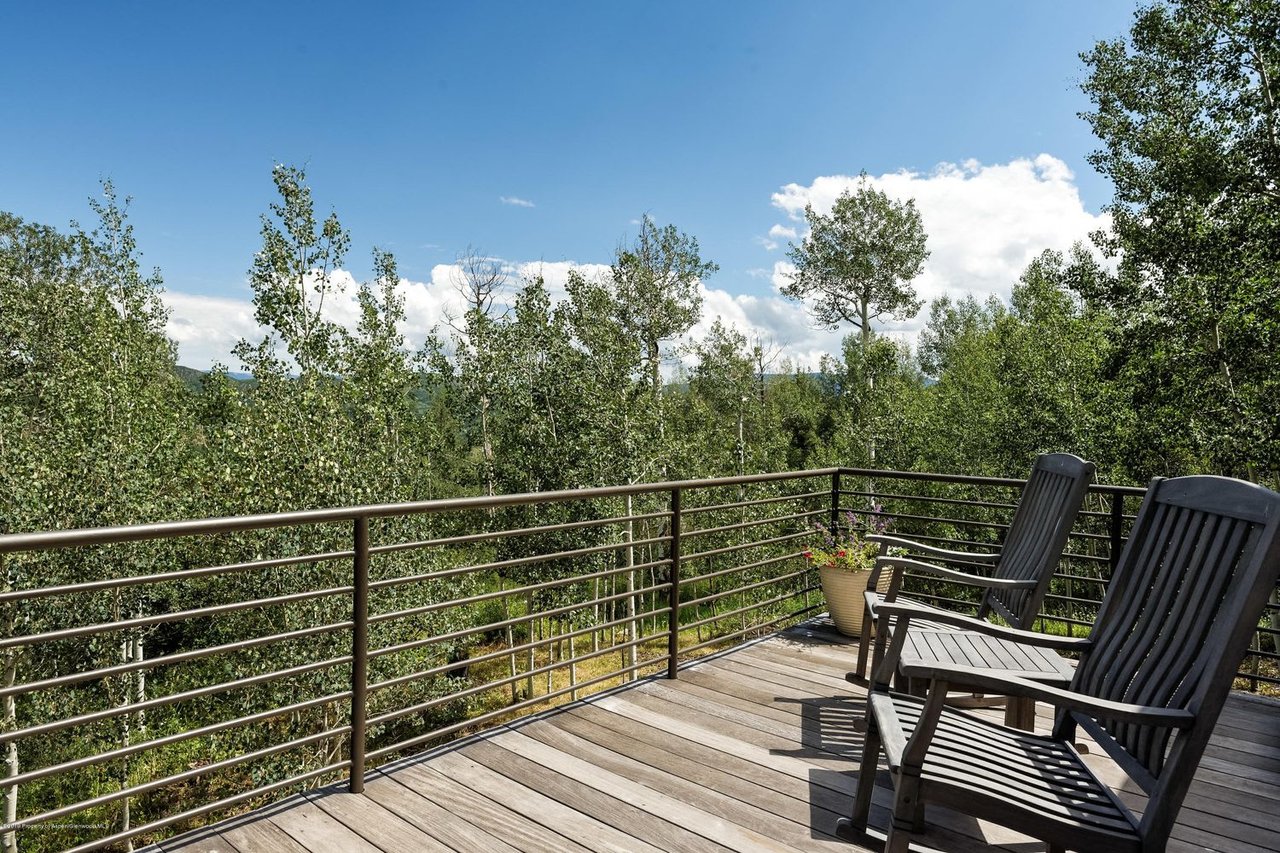 Wooden deck with two Adirondack chairs overlooking leafy trees.