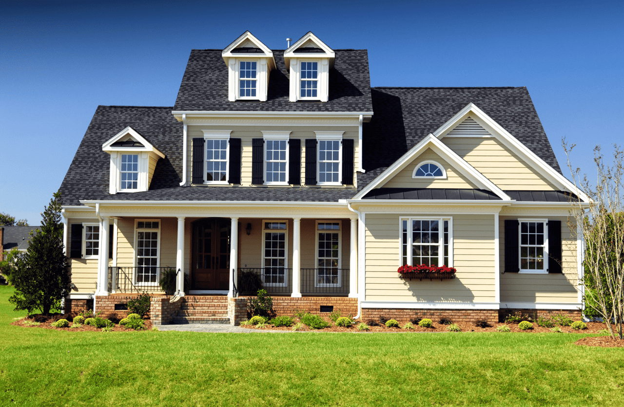 A large house with a black roof and a lot of windows sitting in a grassy field.