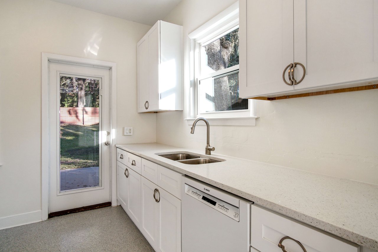 A kitchen view focusing on the sink area, showing white cabinets, a dishwasher, and a window above the sink.
