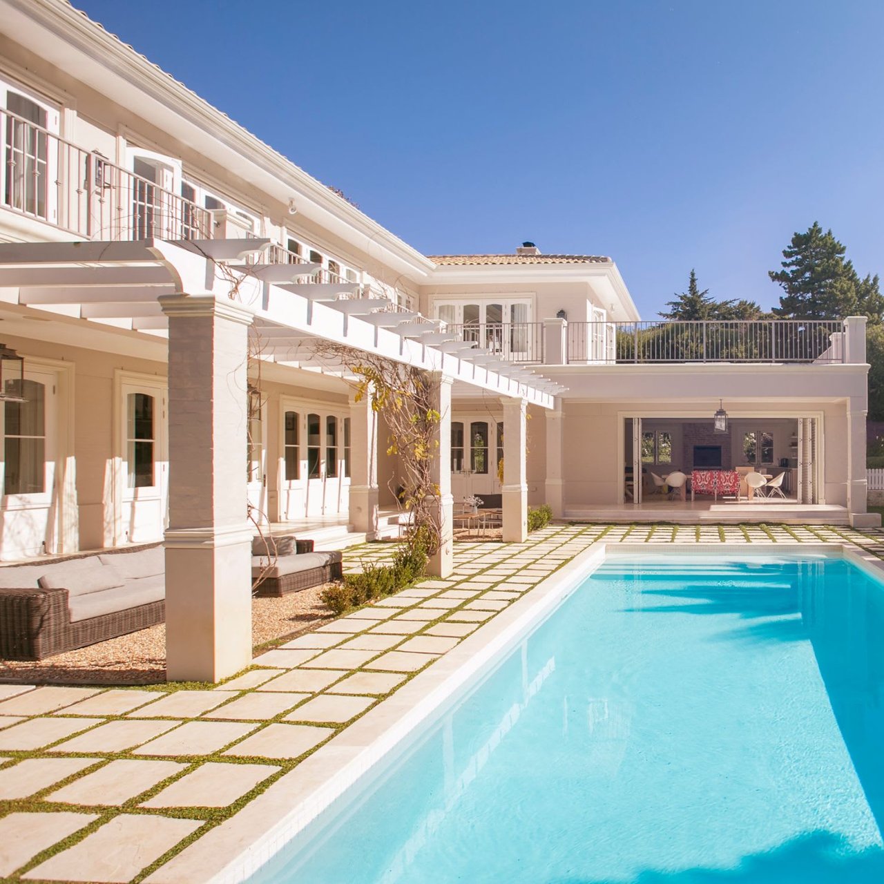 A long, rectangular swimming pool dominates the foreground, with light-colored pavers interspersed with grass leading up to the villa. 