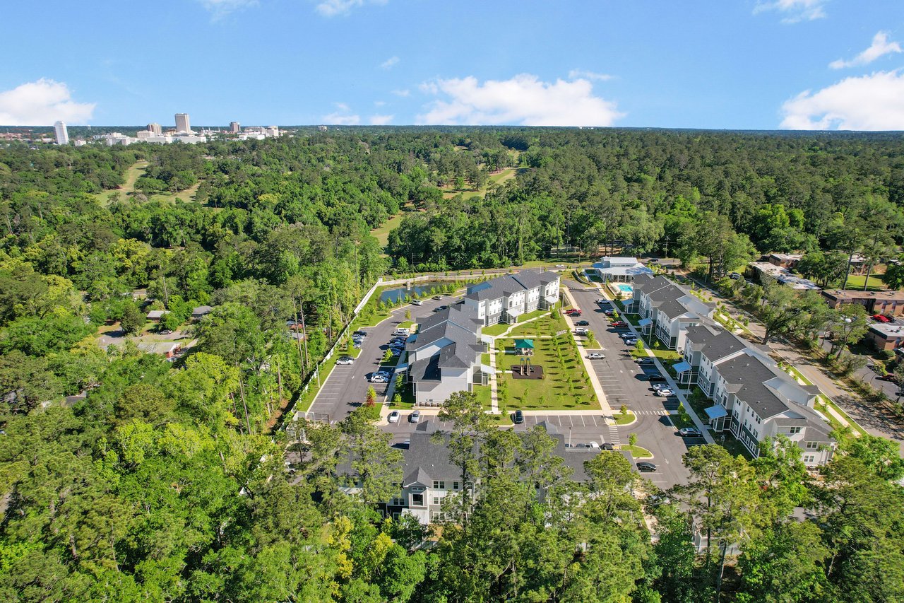 An aerial view of a residential area with rows of houses, streets, and significant green cover.