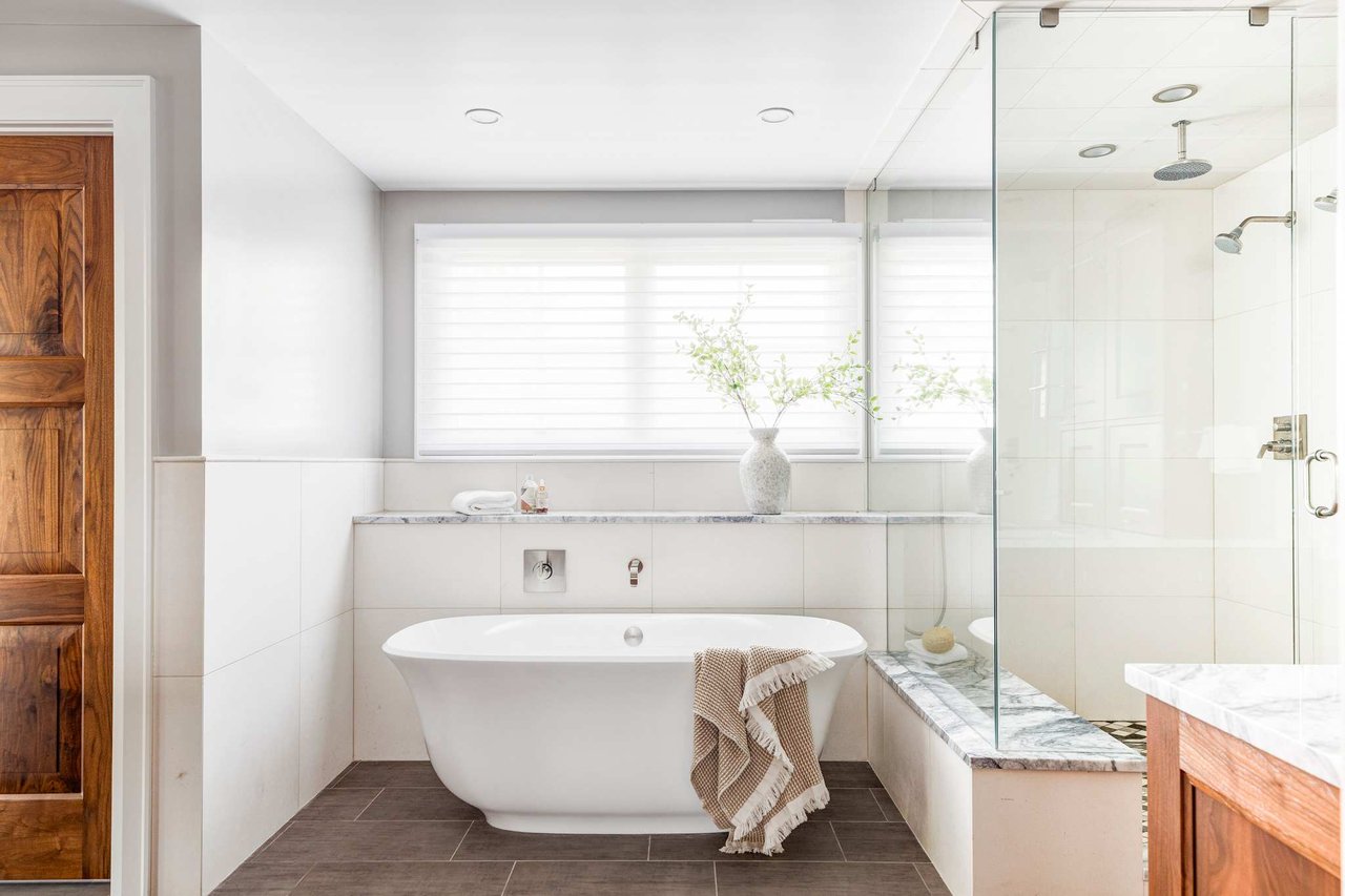 Modern bathroom with freestanding tub, glass shower enclosure, and wood accents