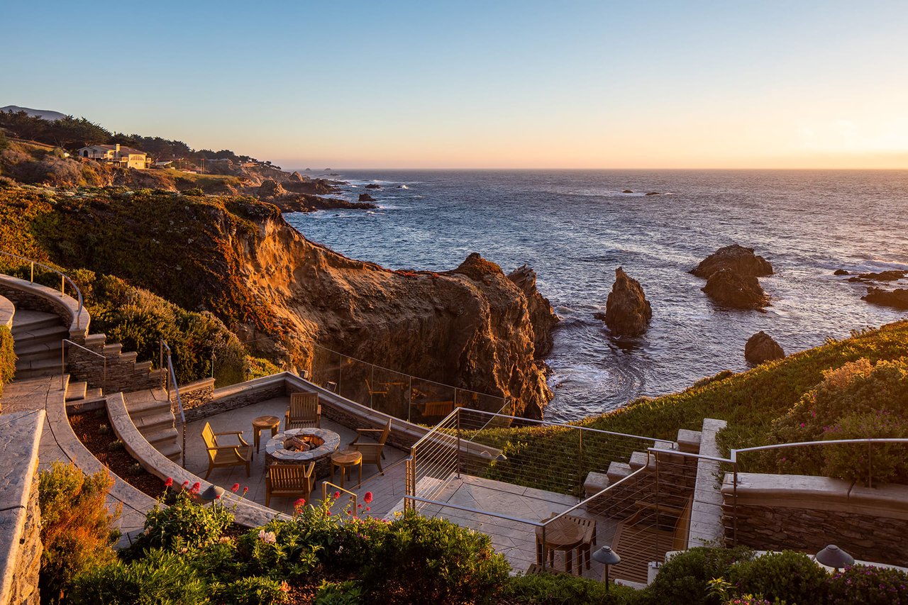 A patio with a fire pit overlooking the ocean at sunset