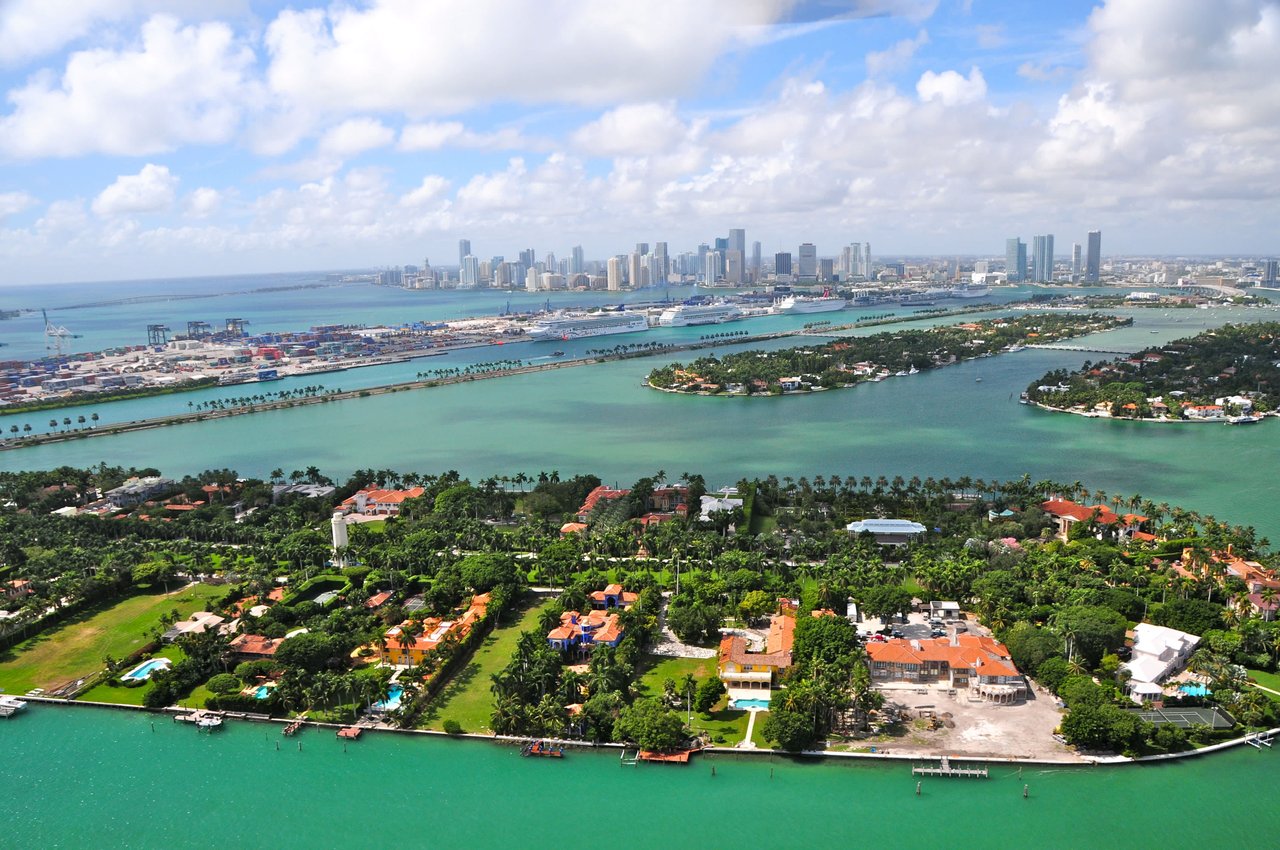 Aerial view of a Venetian Island that has houses on it and is surrounded by a city in the background. 