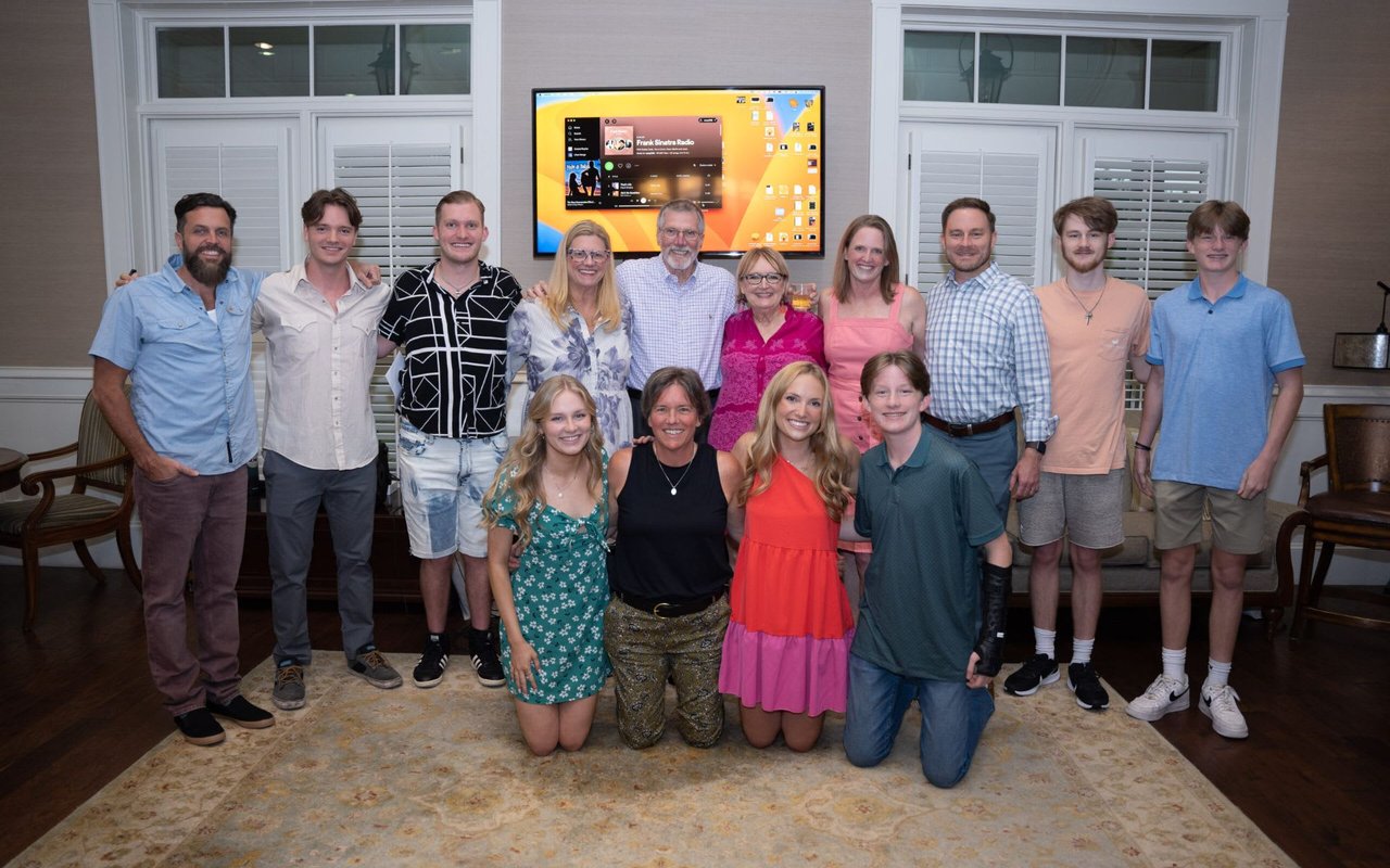  A large group of approximately 14 people, ranging from teenagers to seniors, are posing for a photo in a brightly lit indoor space.