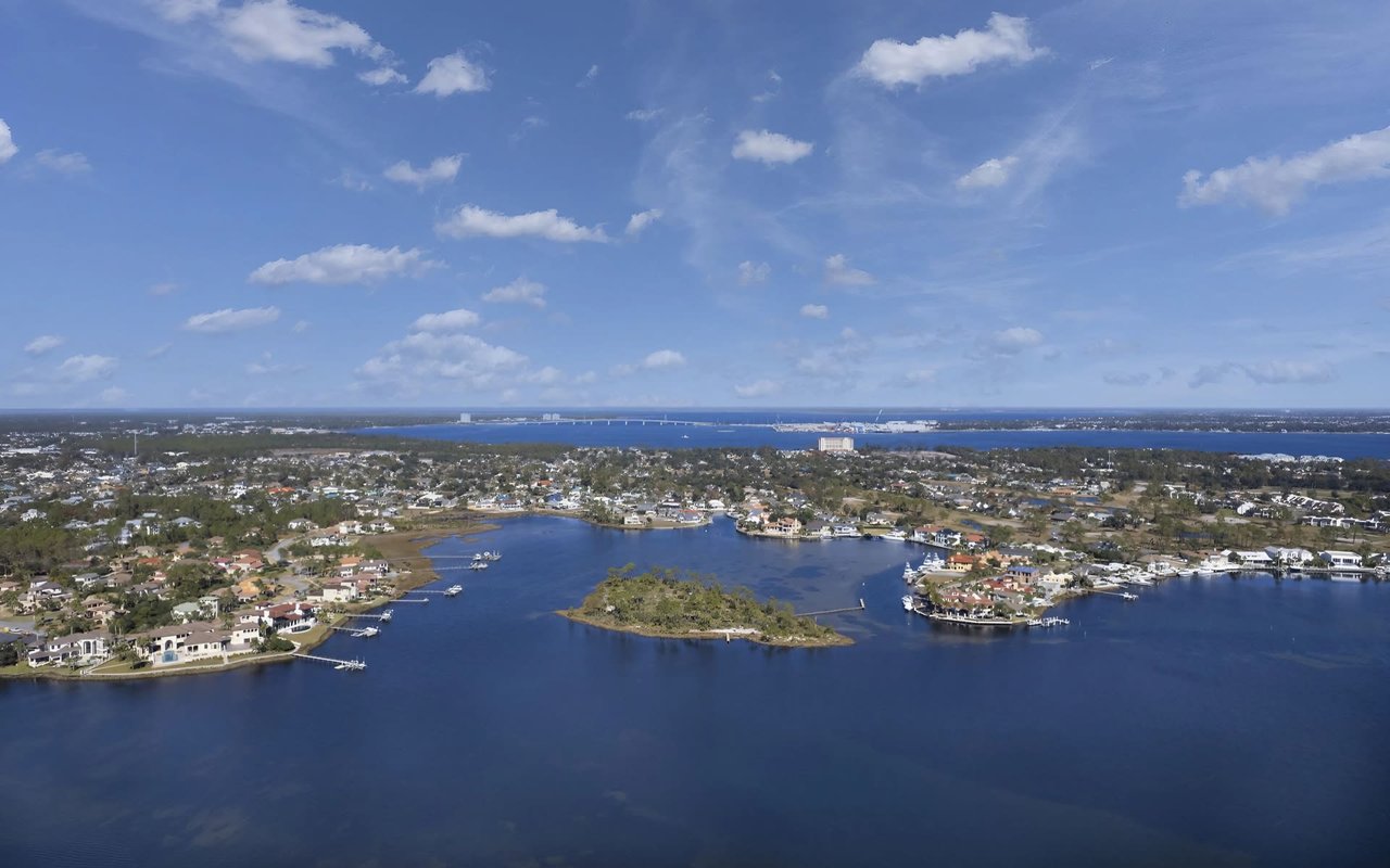 An aerial view of a coastal town with a large body of water, surrounded by residential areas and lush greenery.