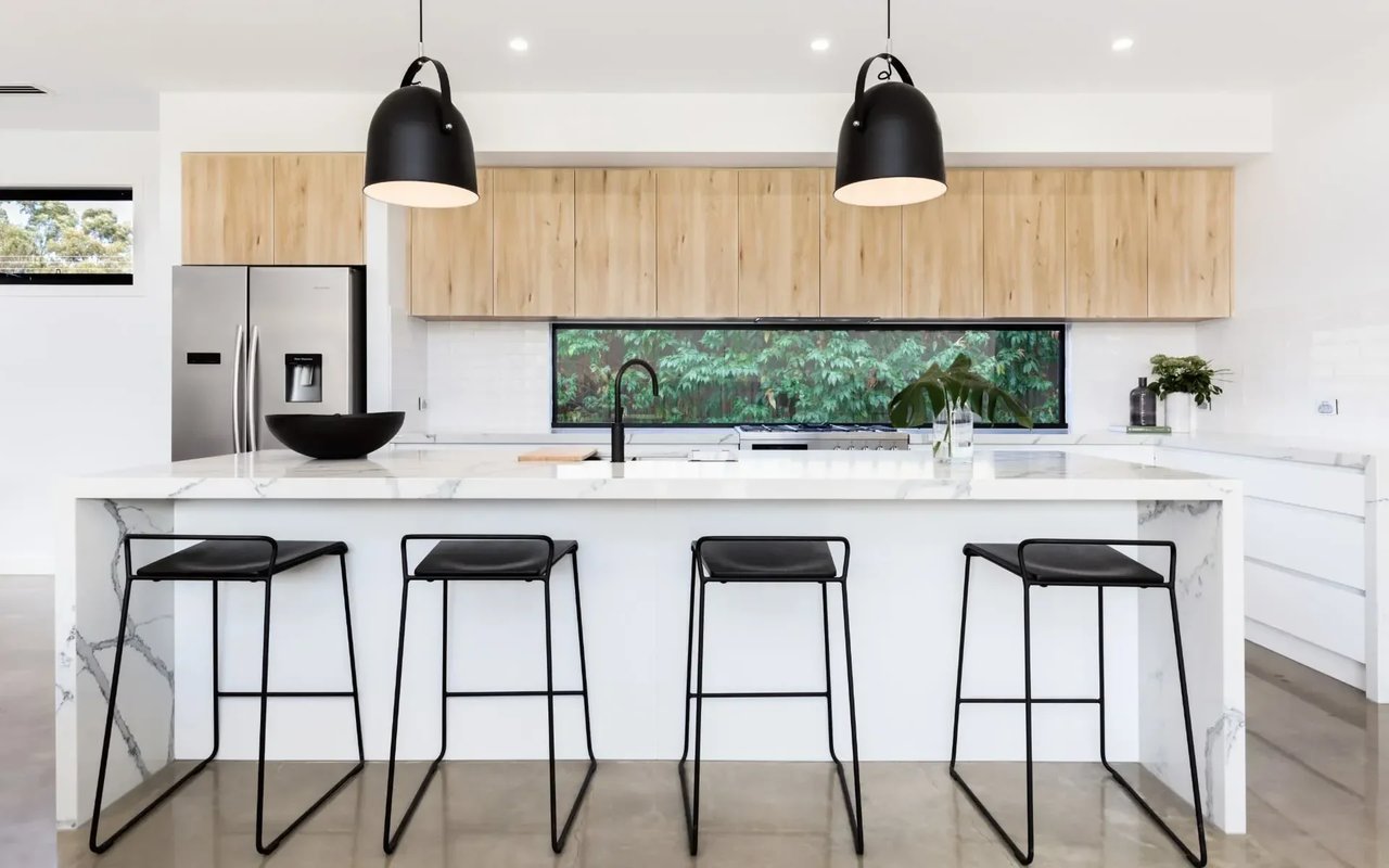 A kitchen with white cabinets, a large marble island with black bar stools, and black pendant lights.