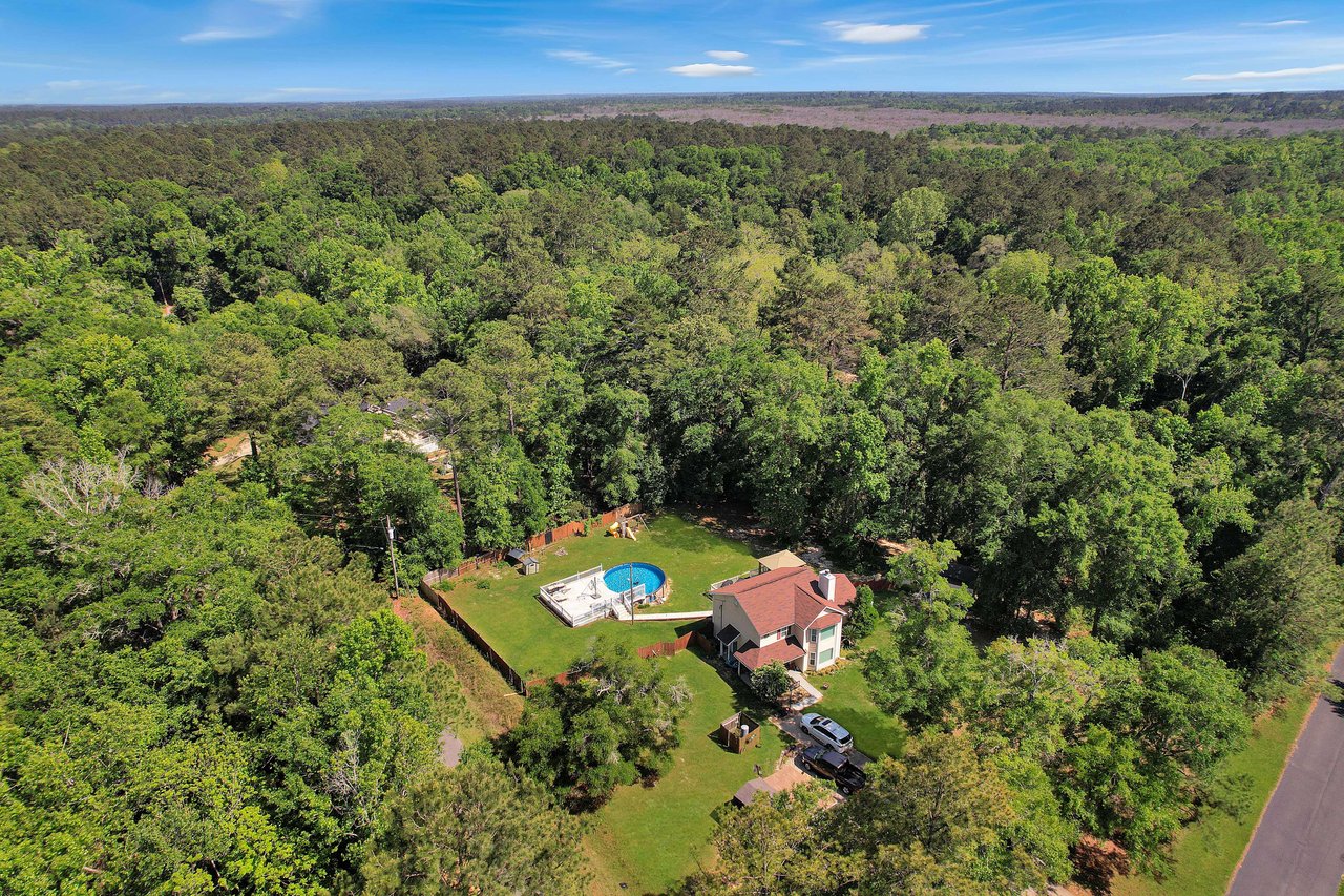 Aerial view of Miccosukee Land Cooperative residential property surrounded by dense forest. A house with a reddish-brown roof and light-colored walls, situated in the lower right corner of the image.