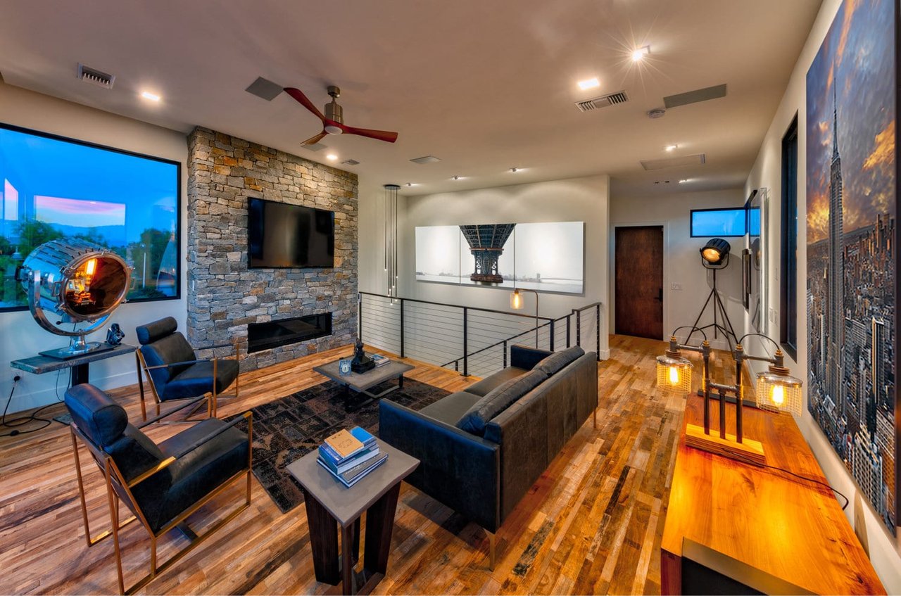 Modern living room with a stone fireplace, leather seating, hardwood floors, and an open stairwell.