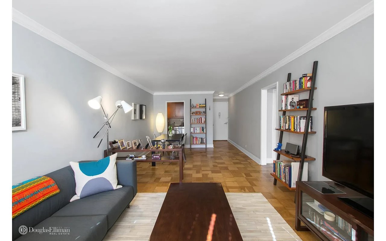 Furnished apartment living room with a gray sofa, parquet floors, and ladder-style bookshelves.