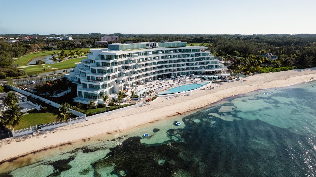  An aerial view captures a large, modern white hotel building with a terraced, stepped design, stretching along a sandy beach. 
