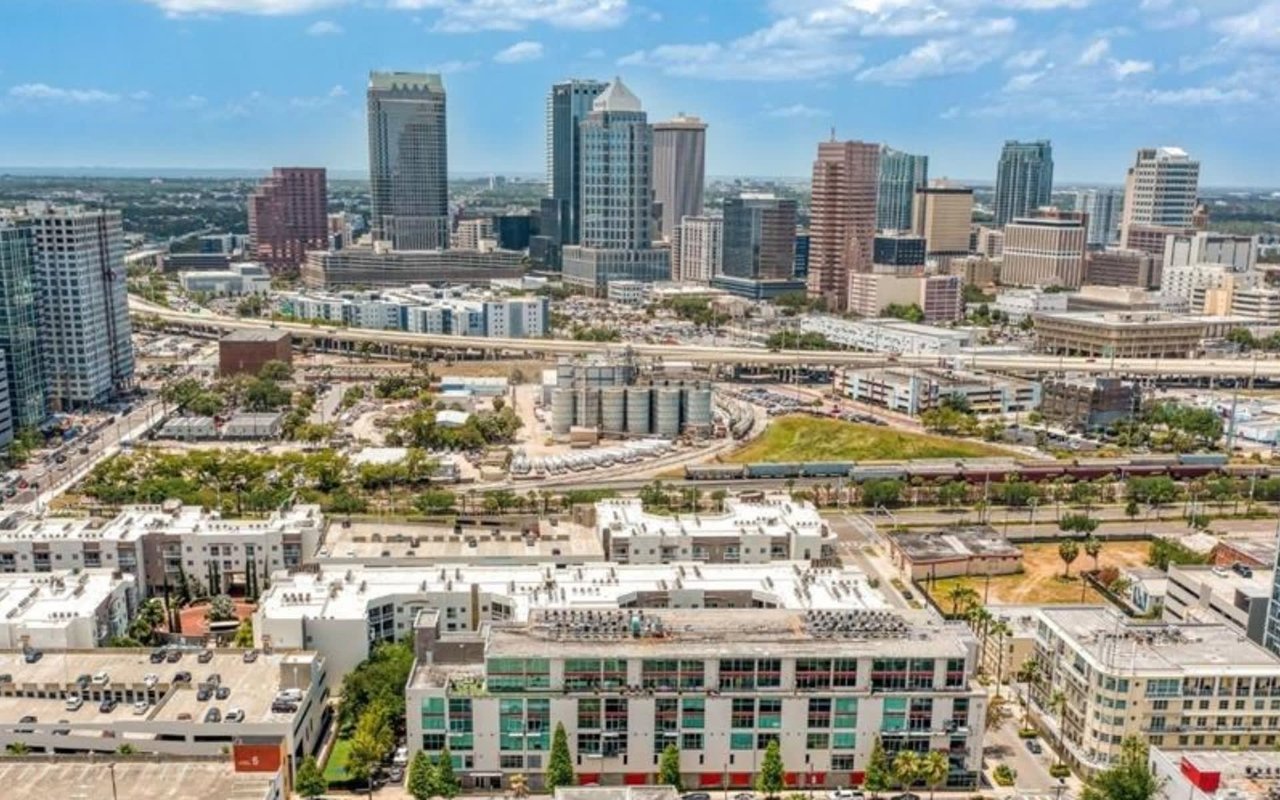 There's a mix of modern residential buildings with light-colored facades and green accents, along with parking lots and roads. 