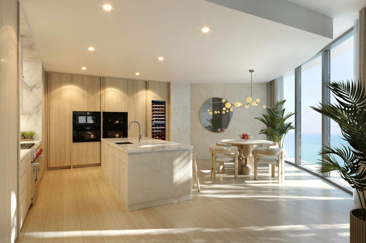 Modern kitchen with a marble island and dining area overlooking the ocean through floor-to-ceiling windows.