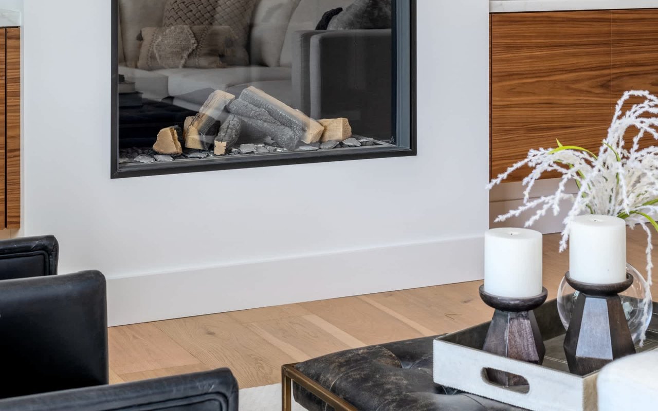 Living room with a glass-front fireplace, light wood floors, and candles on a coffee table.