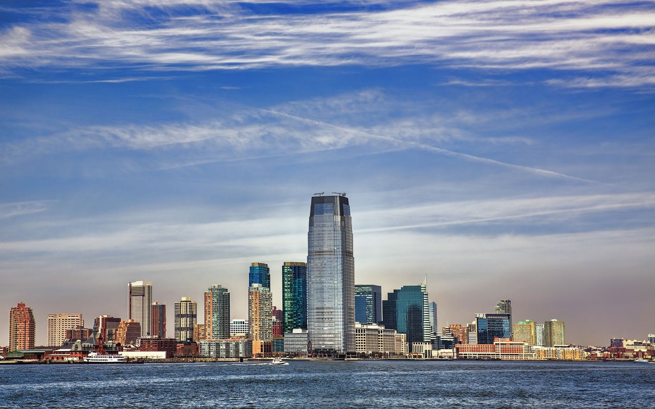 a city skyline consists of tall buildings with illuminated windows from across a body of water at twilight