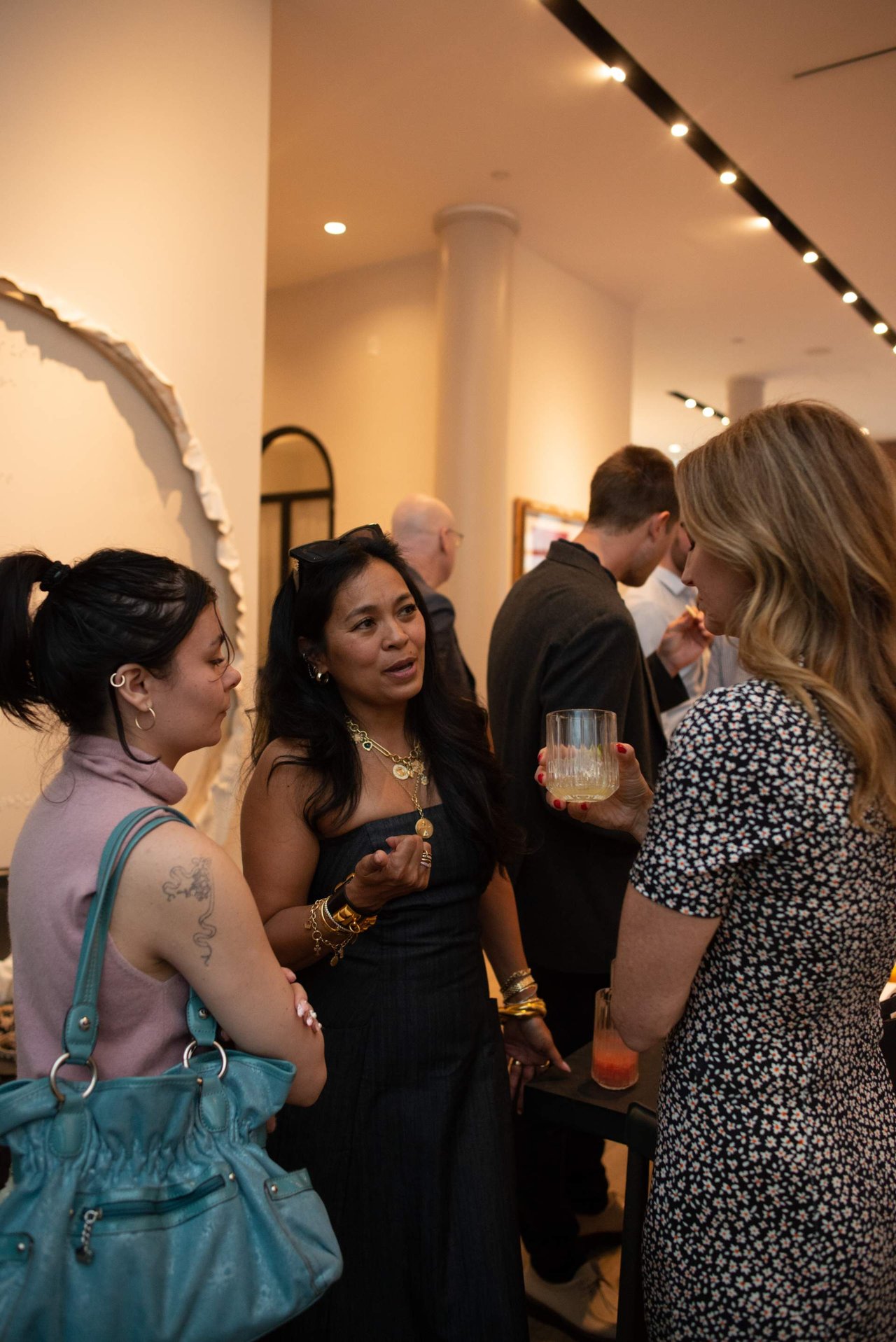 Guests mingle at an indoor event, with three women talking in the foreground.
