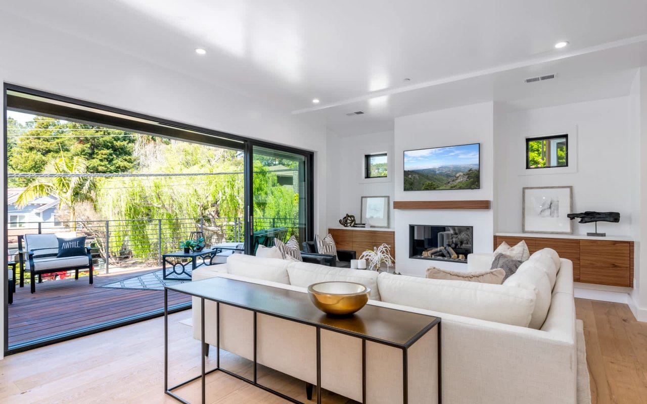 Bright living room with a white sectional, fireplace, and sliding doors opening onto a tree-lined deck.