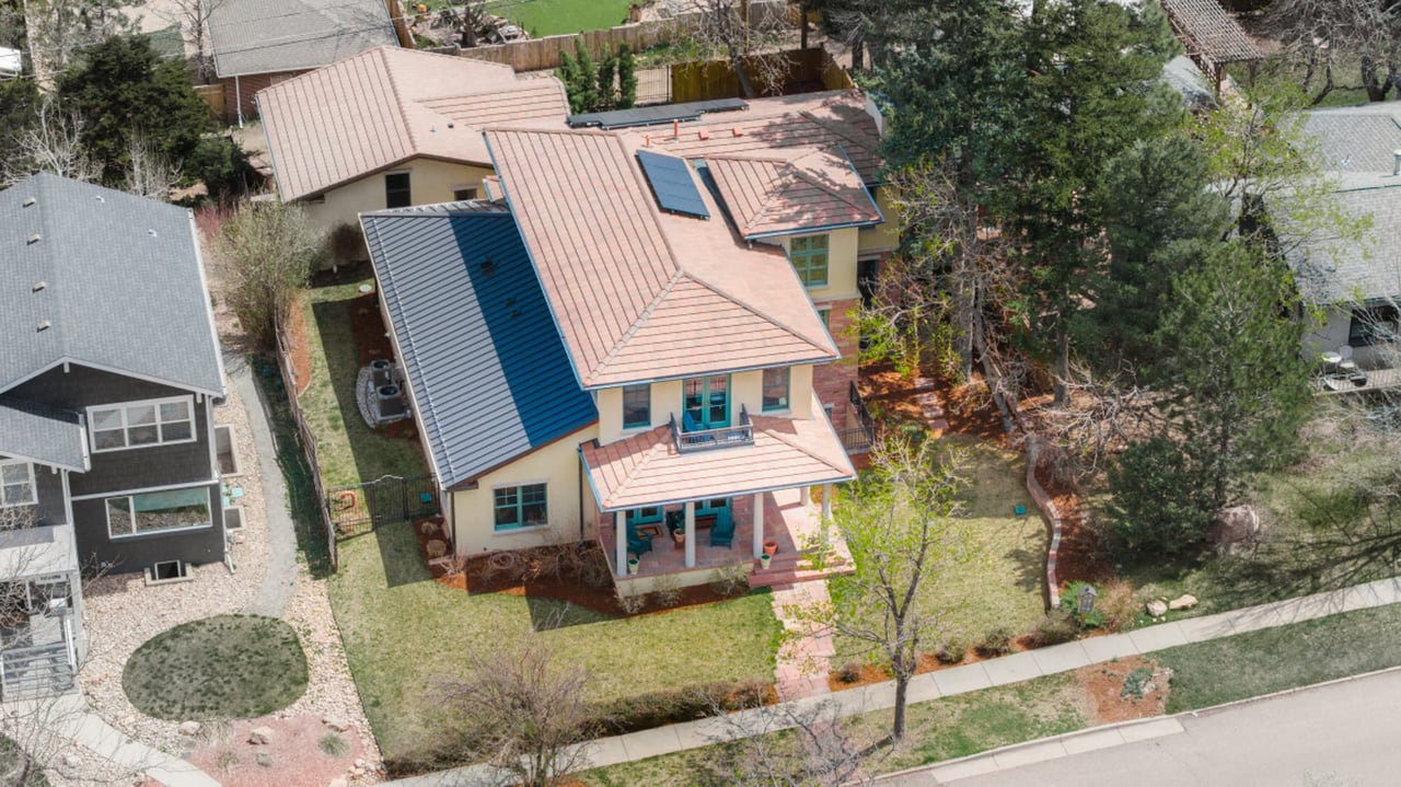 Aerial view of craftsman home with solar panels, terra cotta roof, and landscaped yard