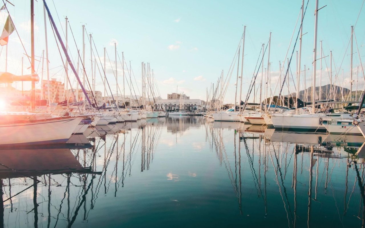 A bustling marina filled with sailboats and yachts with sunsets over the water, casting a warm glow on the scene.