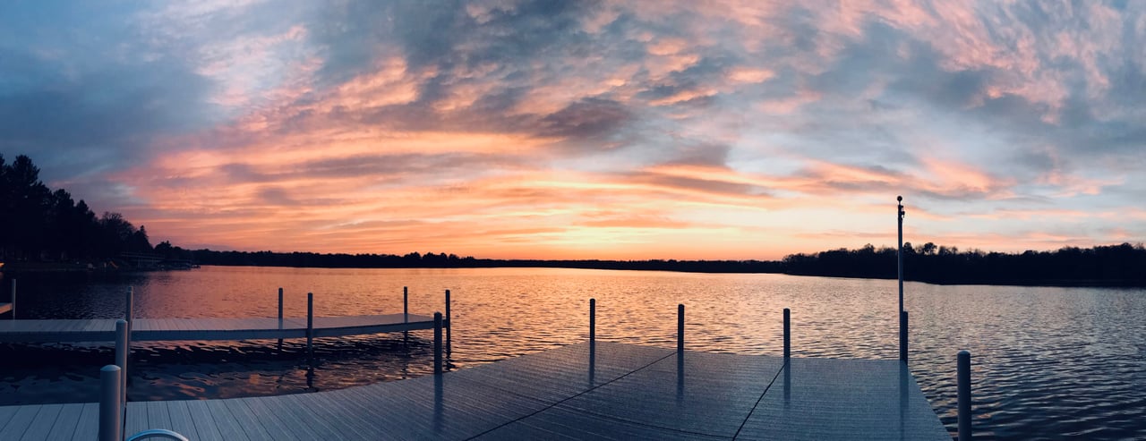 A serene sunset over a lake. The sky is ablaze with hues of orange and pink, reflecting off the still water.