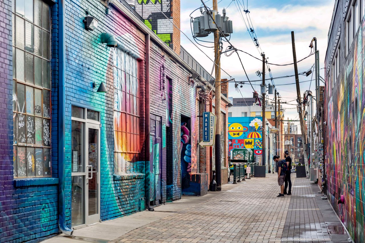 Two people standing in front of the colorful building of Denver central market.