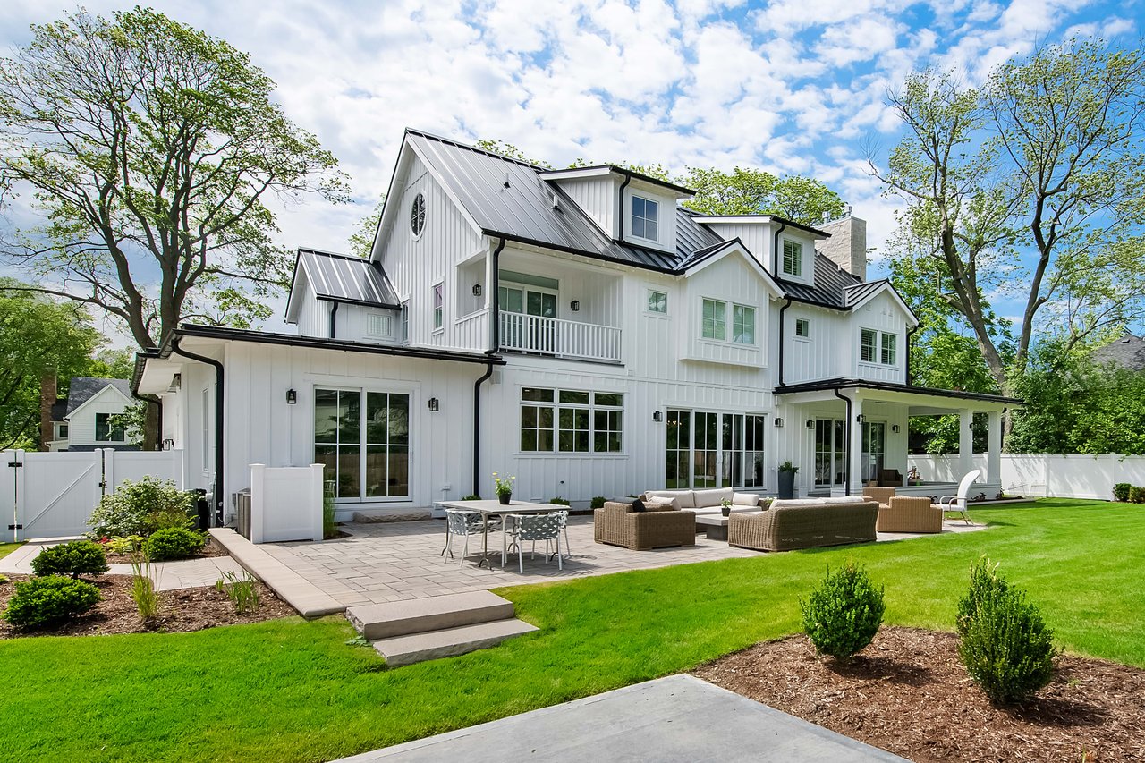 Deck and lawn of a three storied single family home with a white facade and black metallic roof