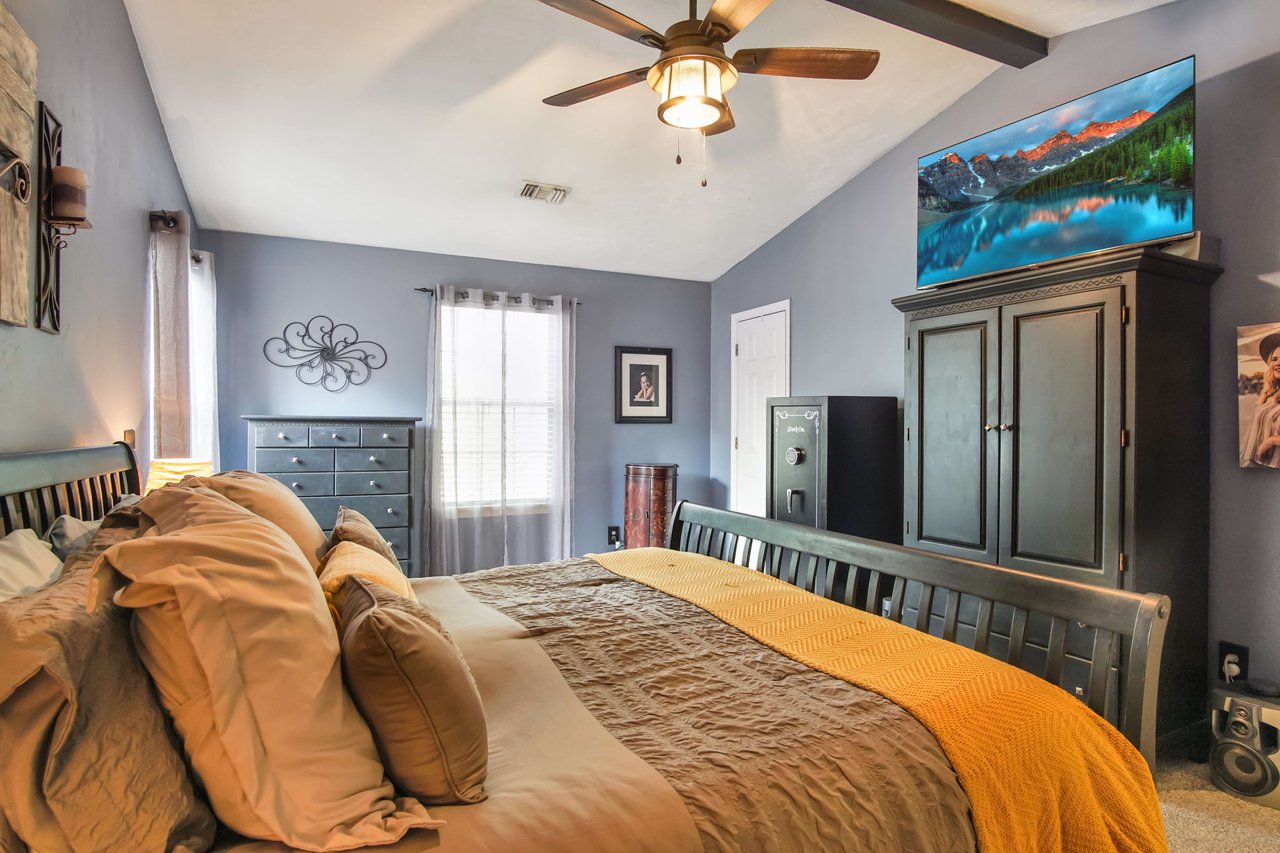 A bedroom with a yellow bedspread, wooden furniture, and blue walls. The room has a ceiling fan, shelves, and is decorated with various items.