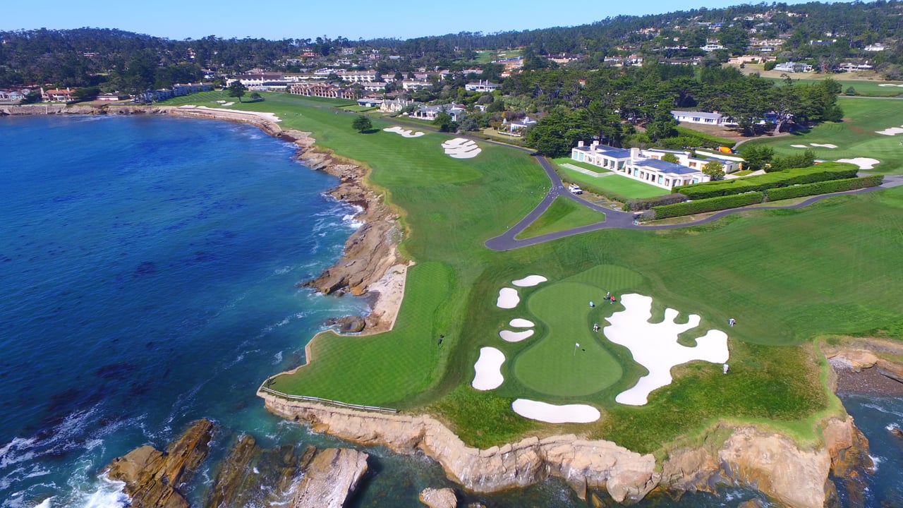 Aerial view of Pebble Beach golf course next to the ocean with a house in the background