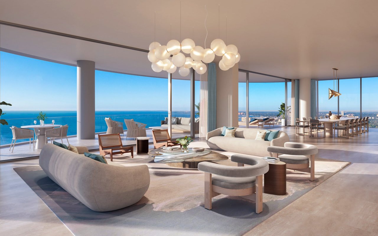 Furnished luxury living room with curved sofas, a sculptural chandelier, and ocean views through floor-to-ceiling windows.