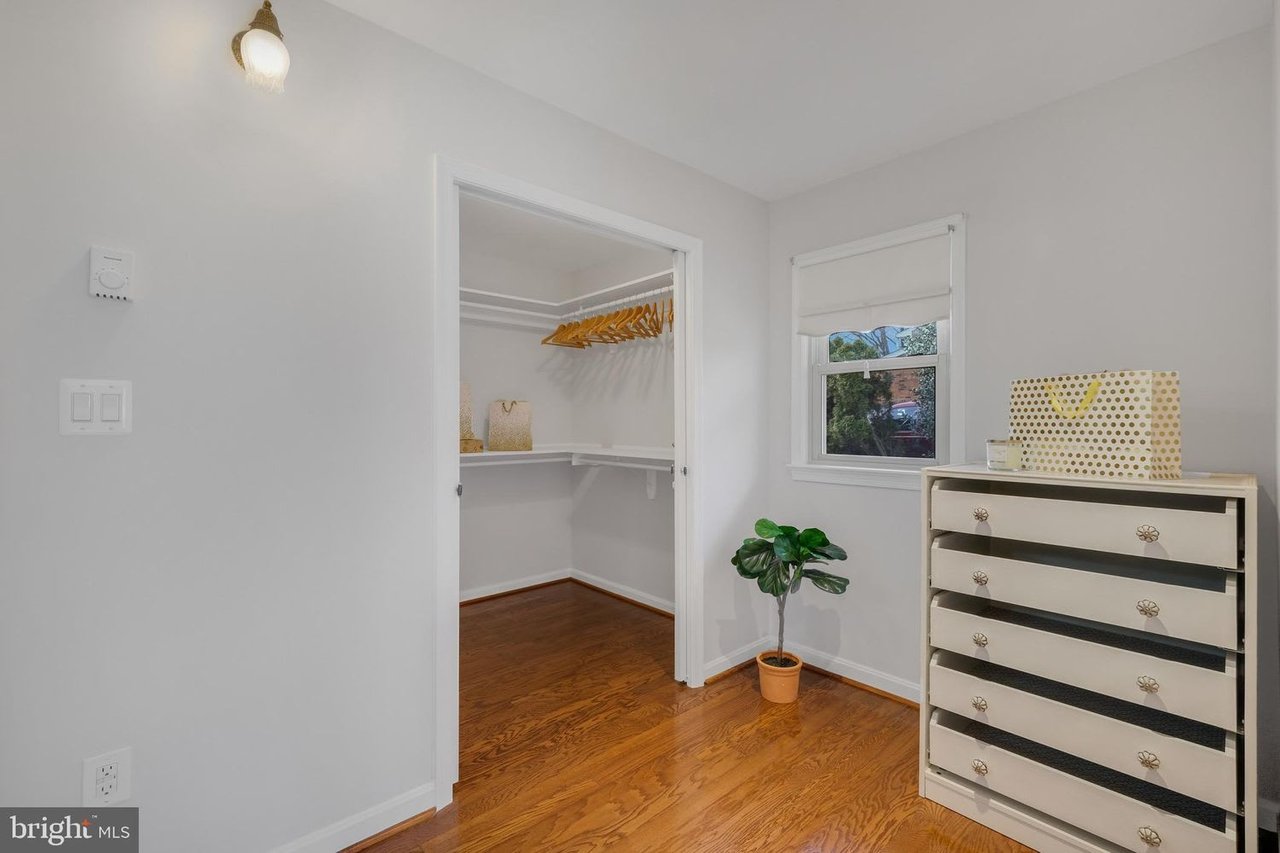 Dressing area with an open walk-in closet, wooden hangers, a white dresser, and hardwood floors.