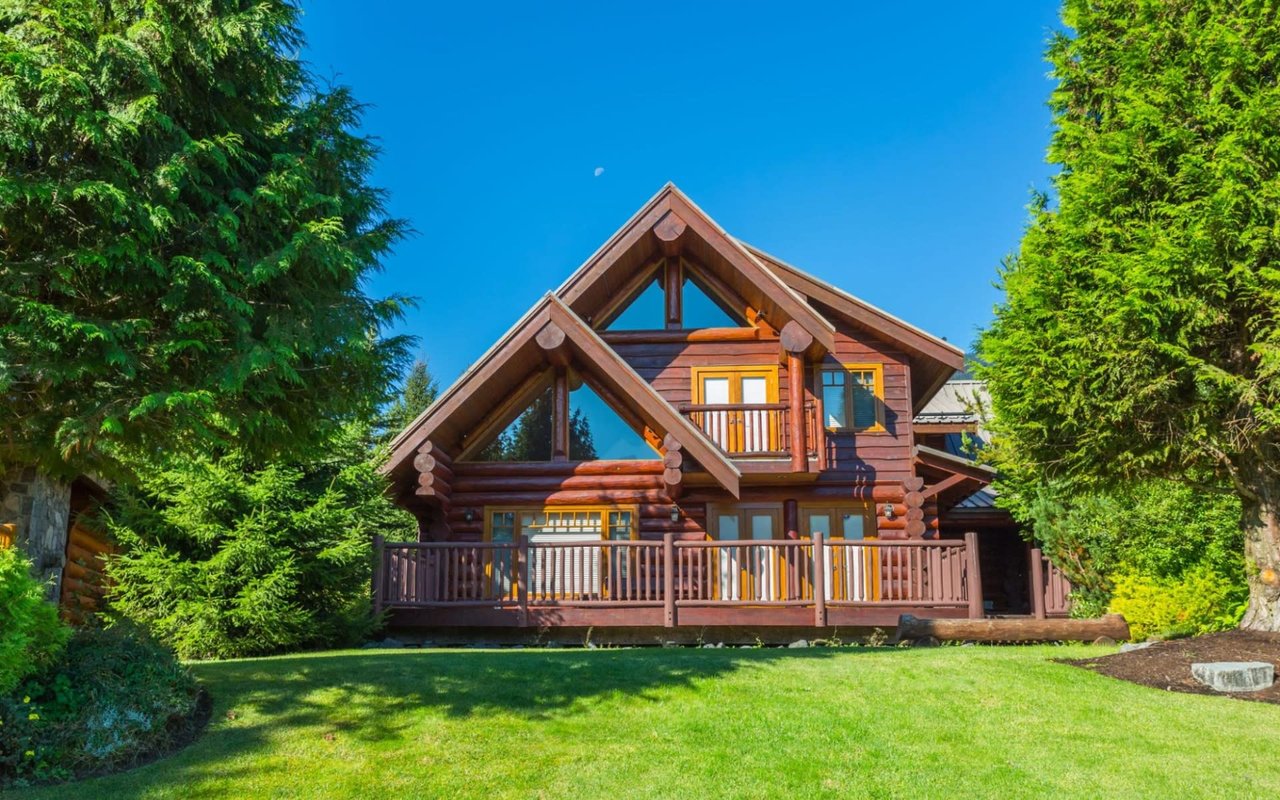 A log cabin with a large wooden deck in the center of a grassy field.