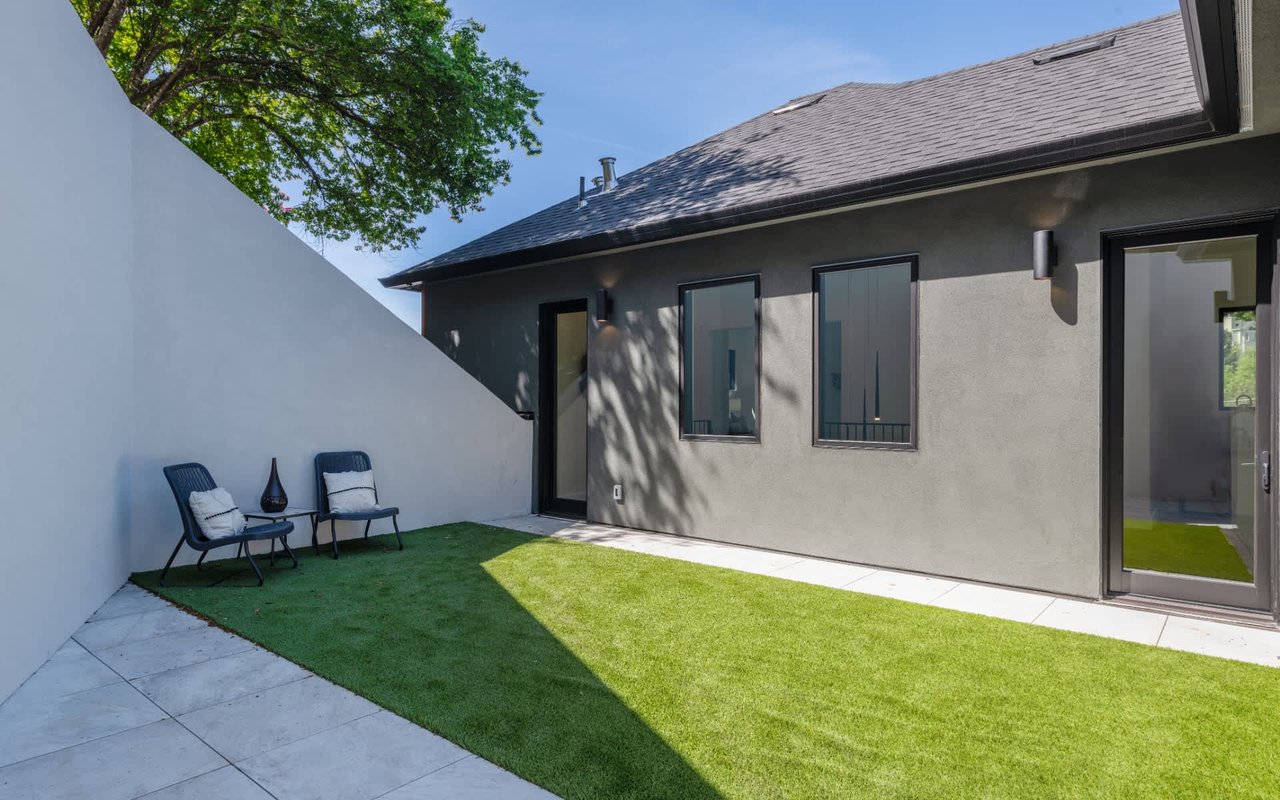 Modern home courtyard with a small lawn, two lounge chairs, and a tall privacy wall.