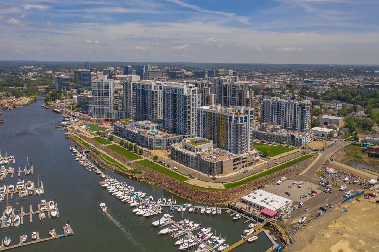 An aerial view of a harbor and a city. The harbor is filled with boats and yachts, and the city is in the background.